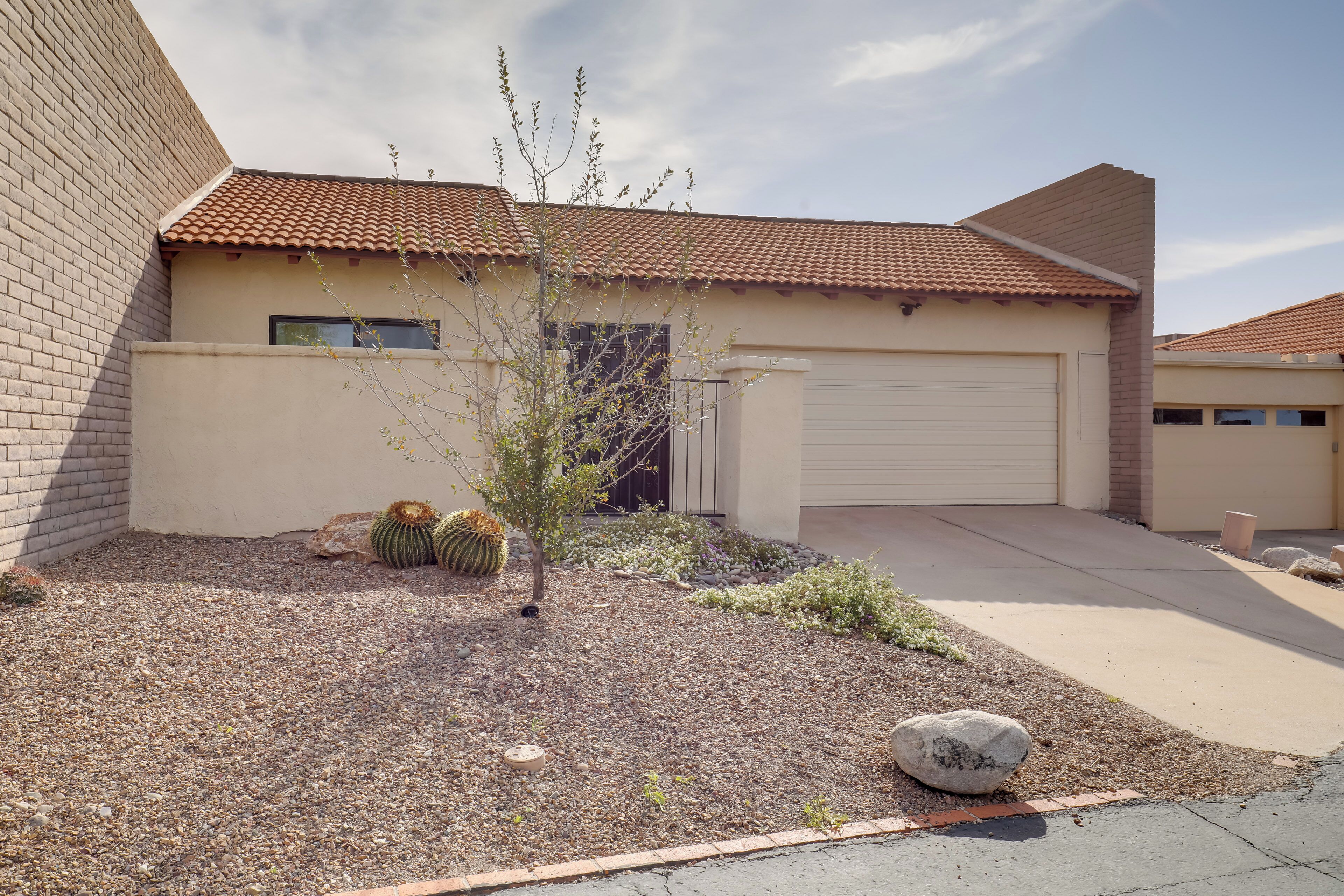 A residential house with a tiled roof, a garage, and a landscaped garden with cacti and a small tree.
