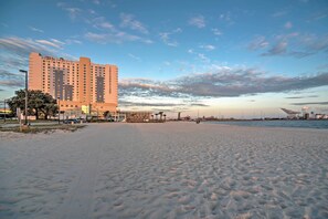 Een hotel aan het strand met een zandstrand, een heldere lucht en een verre blik op industriële gebouwen.