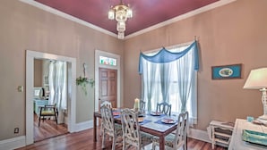A dining room with a wooden table, chairs, and a chandelier. There is a window with blue curtains and a door leading to another room. - Charming Gulfport Getaway Only 3 Blocks to Beach! (Gulfport)