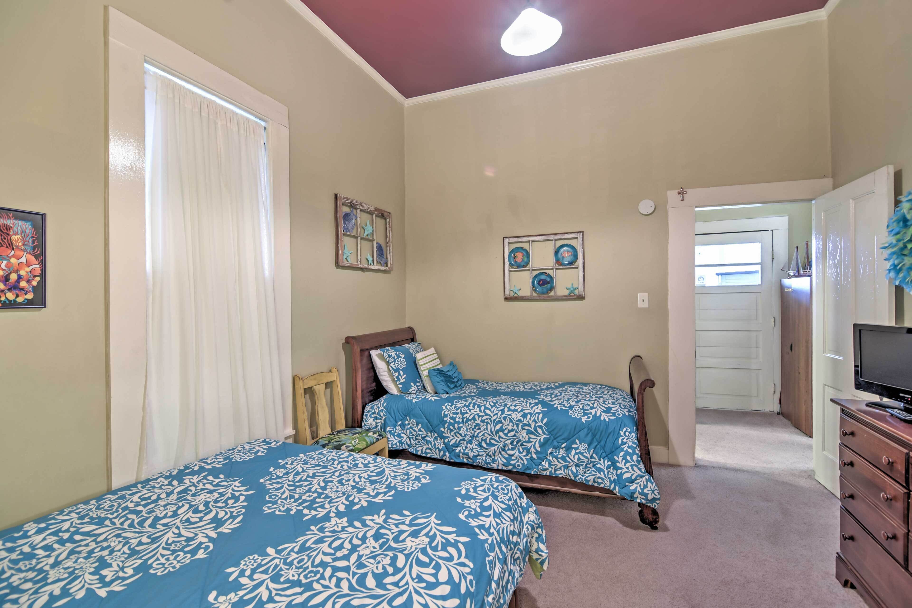 A bedroom with two beds, a dresser, a television, and a door leading to another room.
