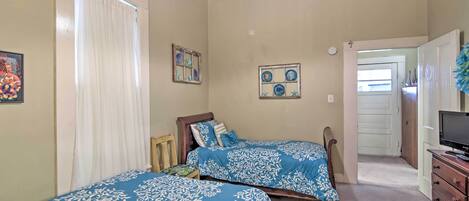 A bedroom with two beds, a dresser, a television, and a door leading to another room.