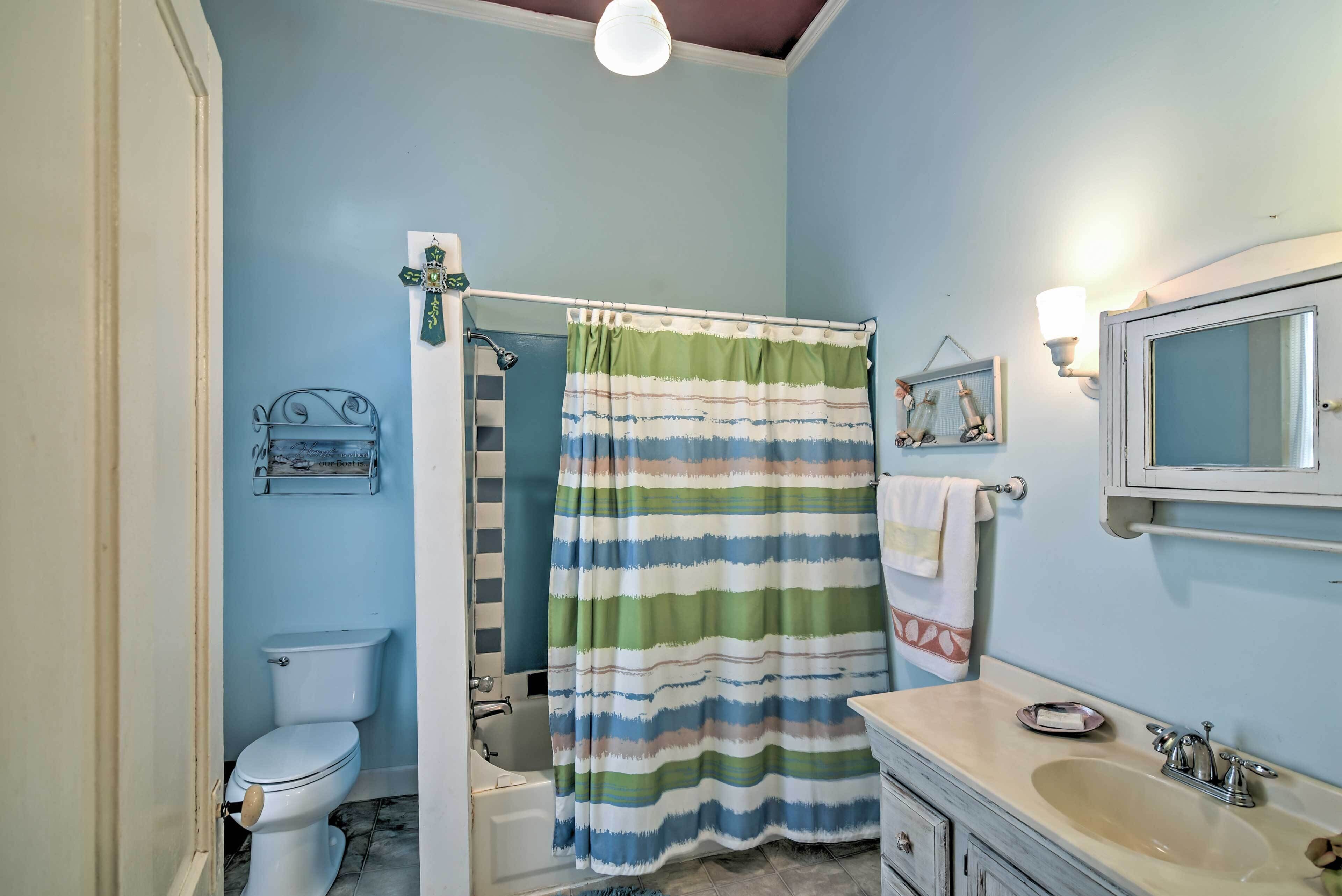 Un baño con cortina de ducha a rayas, inodoro, bañera y lavamanos con espejo.