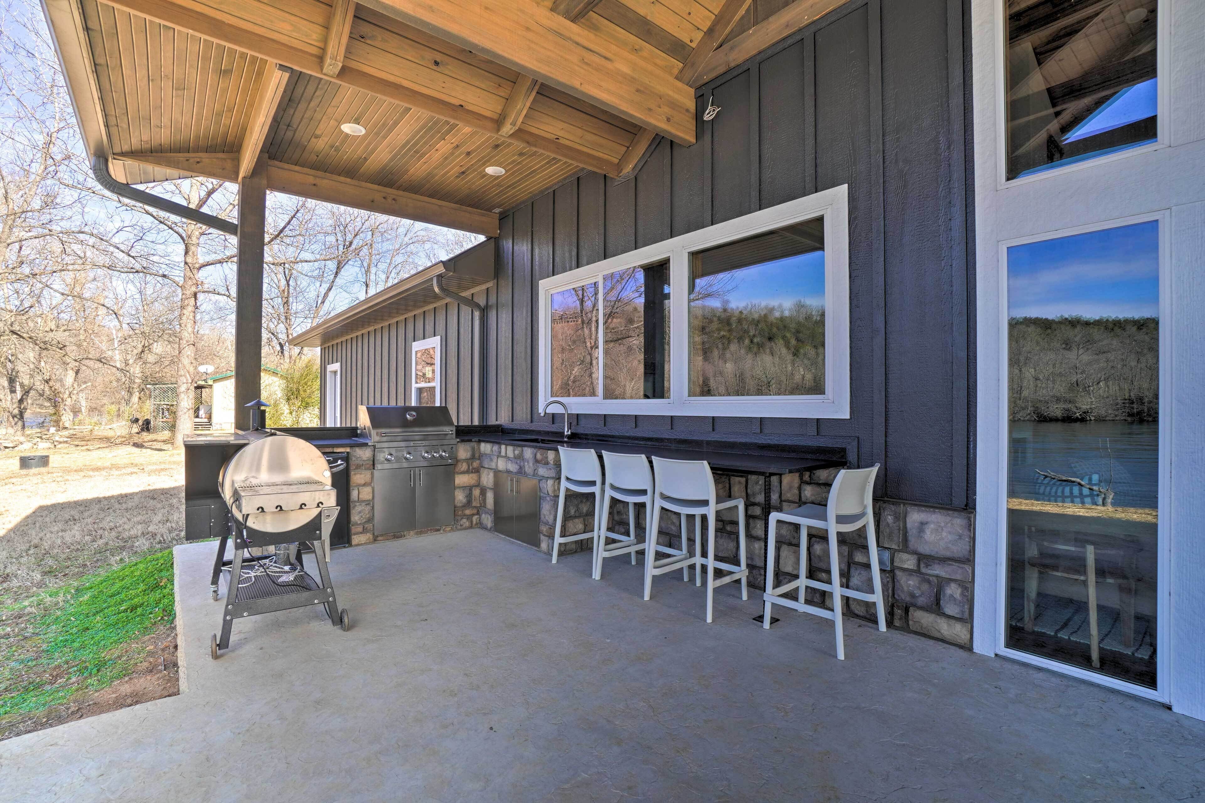 An outdoor patio with a grill, bar stools, and a view of a lake.