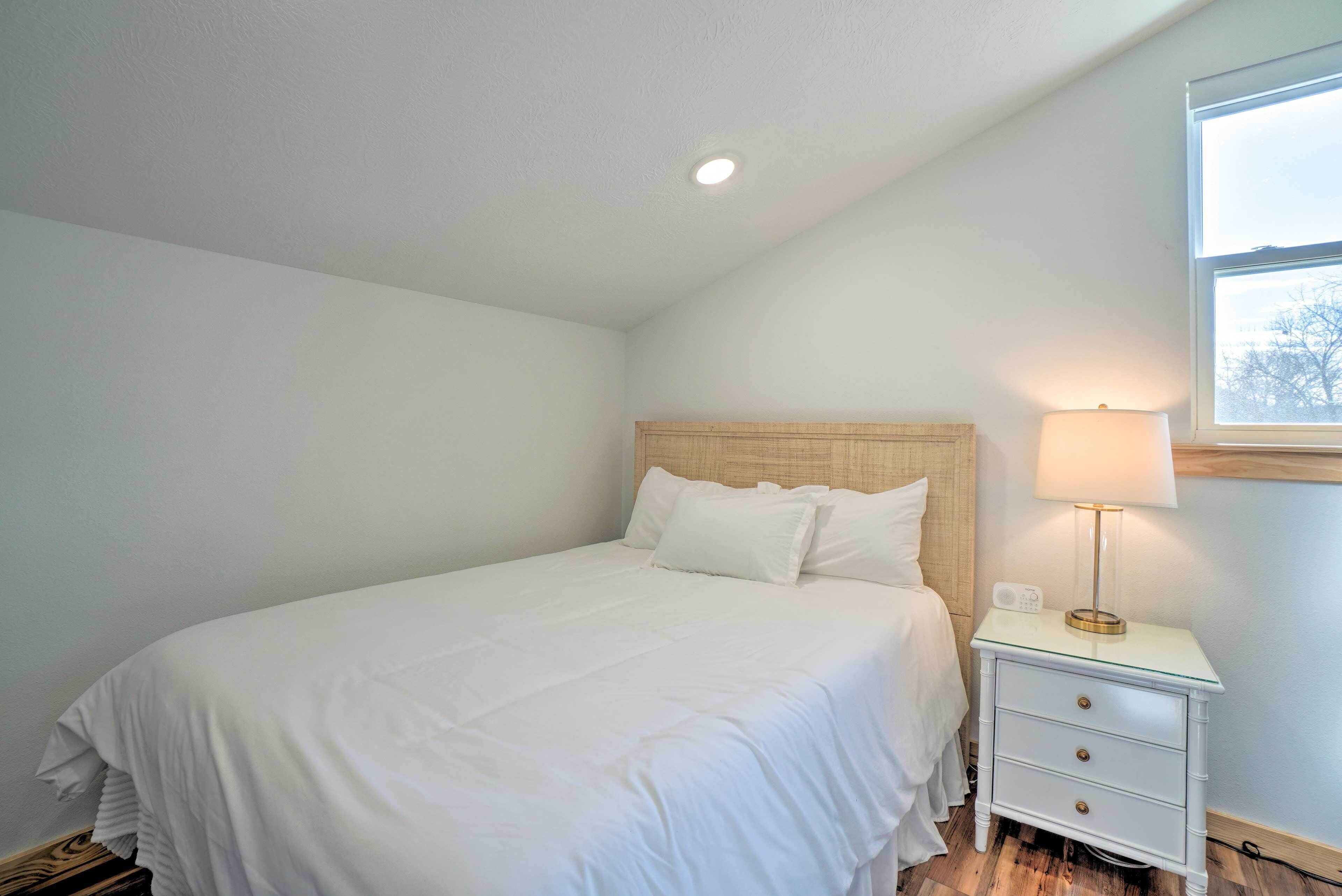A bedroom with a single bed, a nightstand with a lamp, and a window.