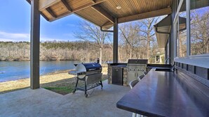 Un patio exterior con una parrilla, chimenea de piedra y vistas a un lago.