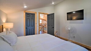 Un dormitorio con una cama, un televisor montado en la pared y un ventilador.