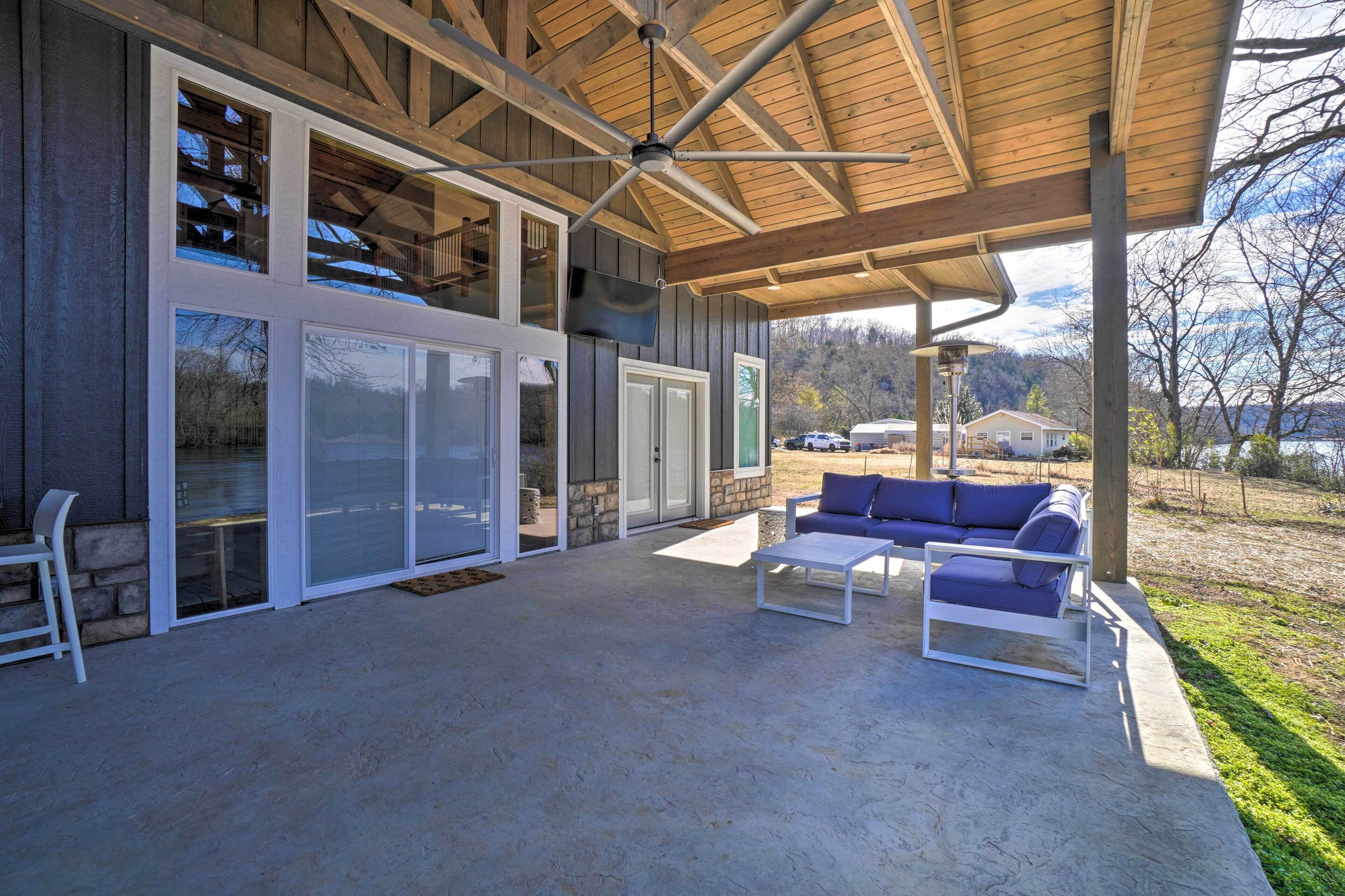 Une terrasse couverte avec un ventilateur de plafond, un mur en pierre et une vue sur un lac.