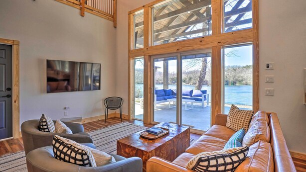 Un salón amplio con un sofá grande, una mesa de centro y un televisor montado en la pared. Una ventana grande ofrece vistas al exterior.