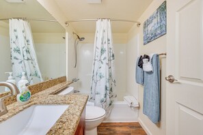 A bathroom with a granite countertop sink, a toilet, a shower with a floral curtain, and a towel rack with towels.