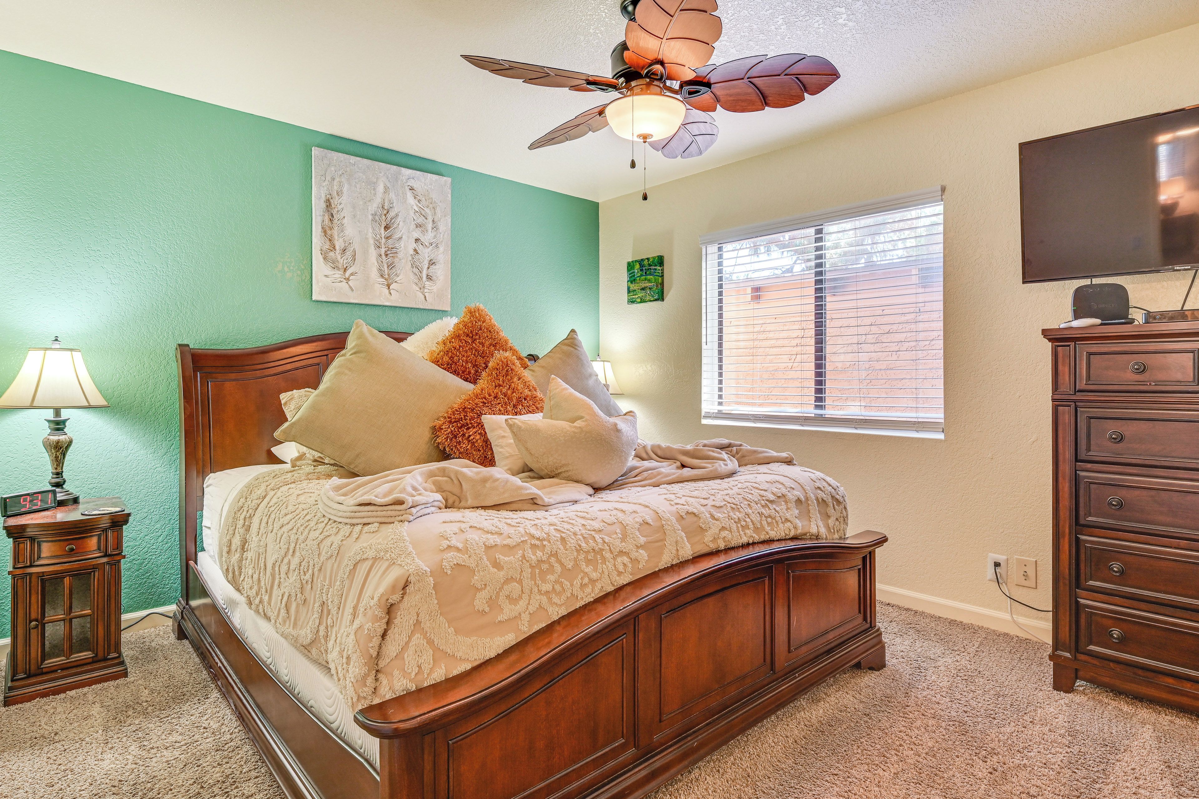 A bedroom with a wooden bed, a ceiling fan, a TV, and a window with blinds.