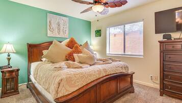 A bedroom with a wooden bed, a ceiling fan, a TV, and a window with blinds.