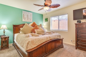 A bedroom with a wooden bed, a ceiling fan, a TV, and a window with blinds.