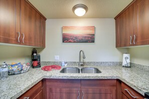 A kitchen with granite countertops, wooden cabinets, a stainless steel sink, and a painting of a sunset.