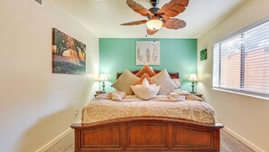Une chambre à coucher avec un lit en bois, deux lampes de chevet, un ventilateur de plafond et des œuvres d’art accrochées aux murs.