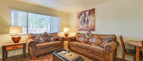 A living room with two brown leather sofas, a coffee table, a rug, a painting, and a dining table with chairs.