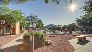 Un espace extérieur ensoleillé avec une piscine, des bancs et un ciel dégagé.