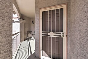 Un balcón con barandilla de madera, una puerta con reja de metal y un muro con textura.