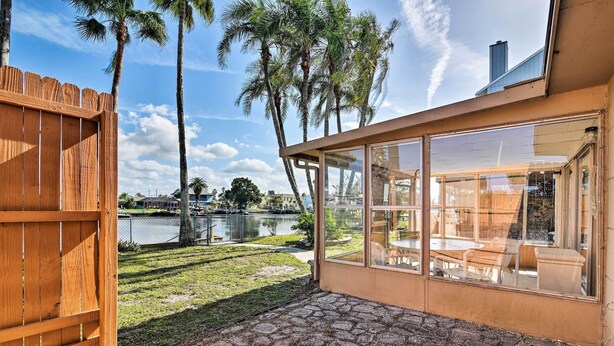 Un patio con piso de piedra, cerca de madera y vista a un lago con palmeras.