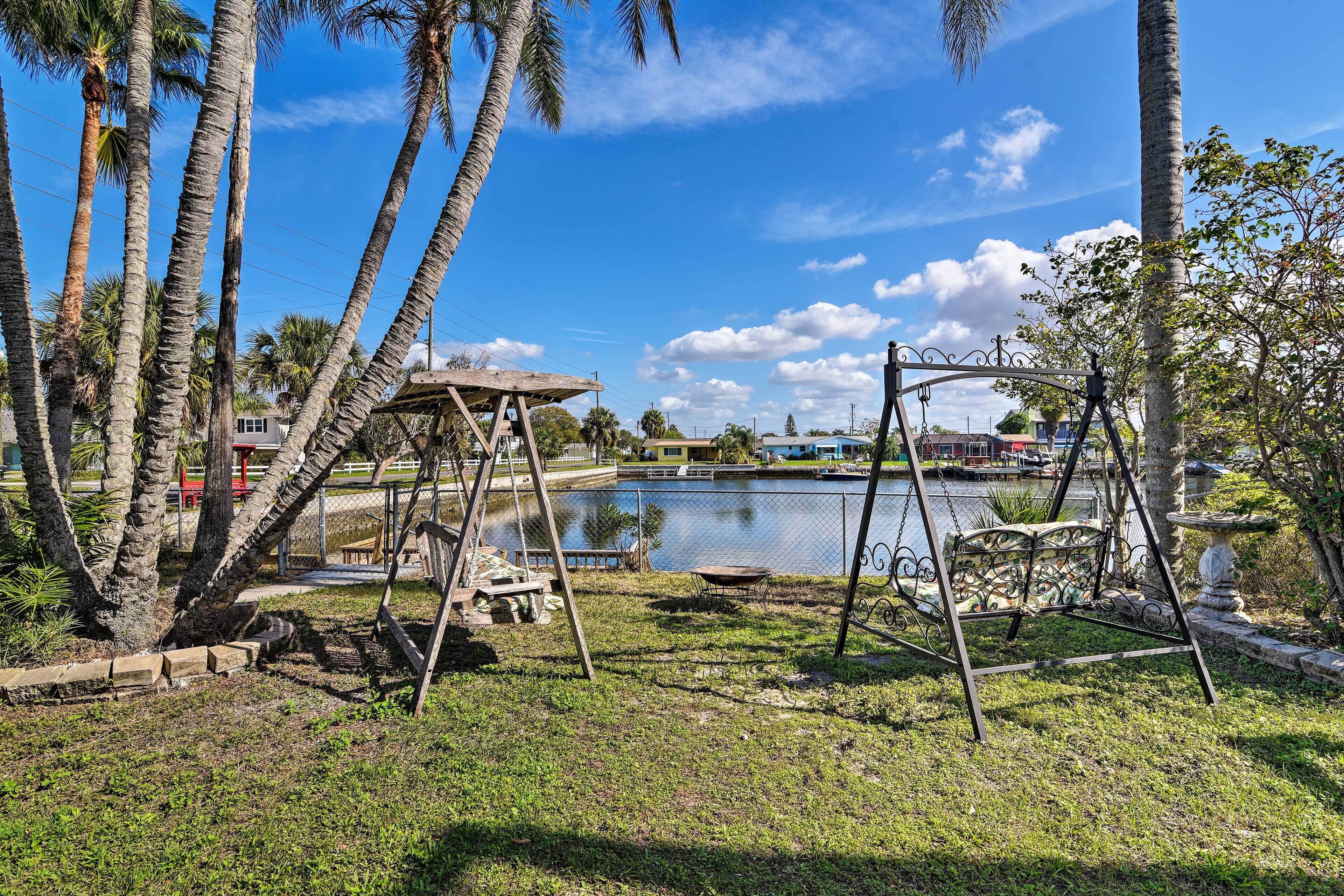 A park with a swing set, a small pond, and palm trees.