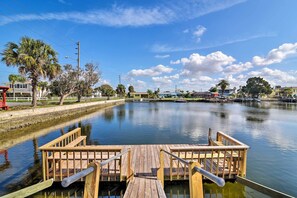 A wooden dock extending into calm water with a clear sky and palm trees in the background.