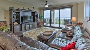 A spacious living room with a leather sofa, a flat-screen TV, and a balcony with a view. - Ornate Resort Condo w/ Balcony, Pool, Water Views! (Pensacola)