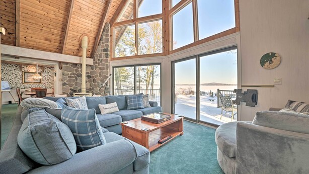 A spacious living room with a high wooden ceiling, stone walls, and large windows offering a view of the outdoors.