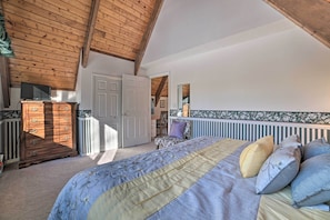 A bedroom with a wooden ceiling, a bed with a floral bedspread, a dresser, and a white door.