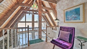 A high-ceilinged room with a wooden staircase, a purple chair, and a painting on the wall.