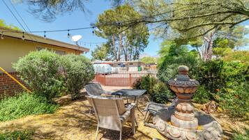 A backyard with outdoor furniture, a stone fountain, and a house in the background.