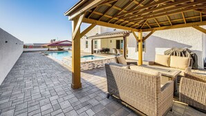 Un patio exterior con piscina, mobiliario de mimbre y una zona de estar cubierta.