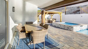 Un patio exterior con piscina, mobiliario de mimbre y una pérgola.