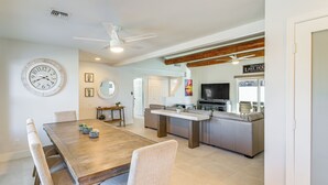 Amplia sala de estar con mesa de comedor, asientos, cocina y un reloj grande en la pared.