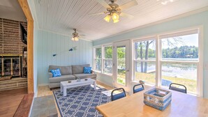 A spacious living room with a large window, a fireplace, and a ceiling fan. - Lakefront Wisconsin Cottage w/ Dock & Hot Tub! (Pound)
