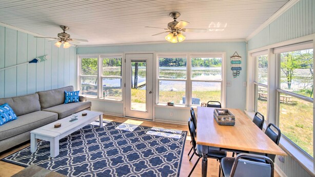 A spacious room with a large window, a ceiling fan, a wooden dining table, and a sofa with blue cushions. - Lakefront Wisconsin Cottage w/ Dock & Hot Tub! (Pound)