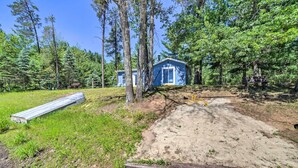 A rustic cabin surrounded by dense forest, with a dirt path leading to the entrance. - Lakefront Wisconsin Cottage w/ Dock & Hot Tub! (Pound)