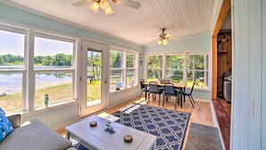 A spacious room with large windows overlooking a lake, a dining area with a table and chairs, and a ceiling fan. - Lakefront Wisconsin Cottage w/ Dock & Hot Tub! (Pound)