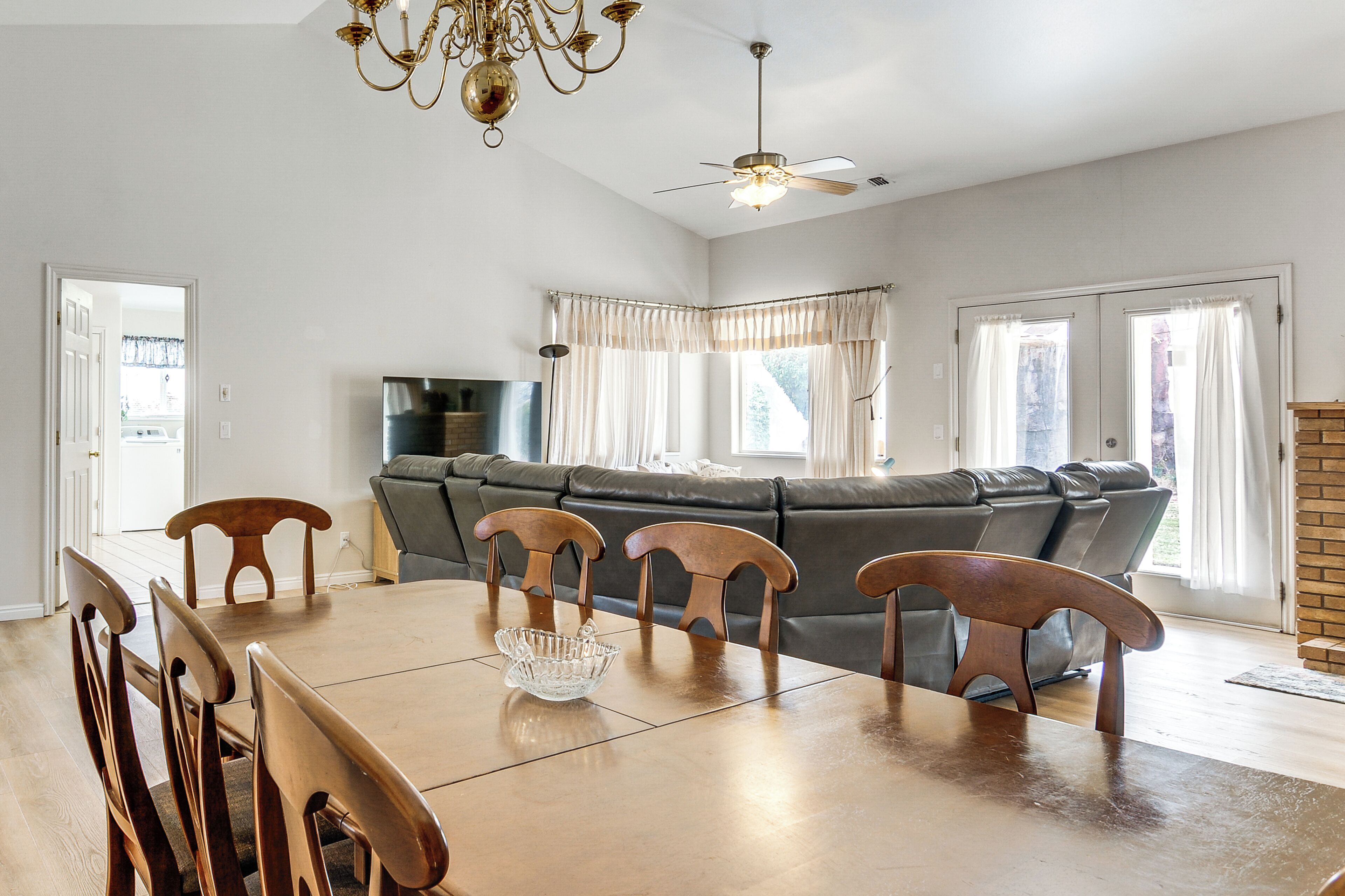 Un coin repas avec une table en bois, des chaises, un lustre et un ventilateur de plafond.