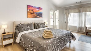 A bedroom with a bed, a nightstand, a lamp, a painting, and a window with curtains.