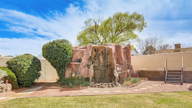 A landscaped garden with a rock formation, a tree, and a paved pathway.