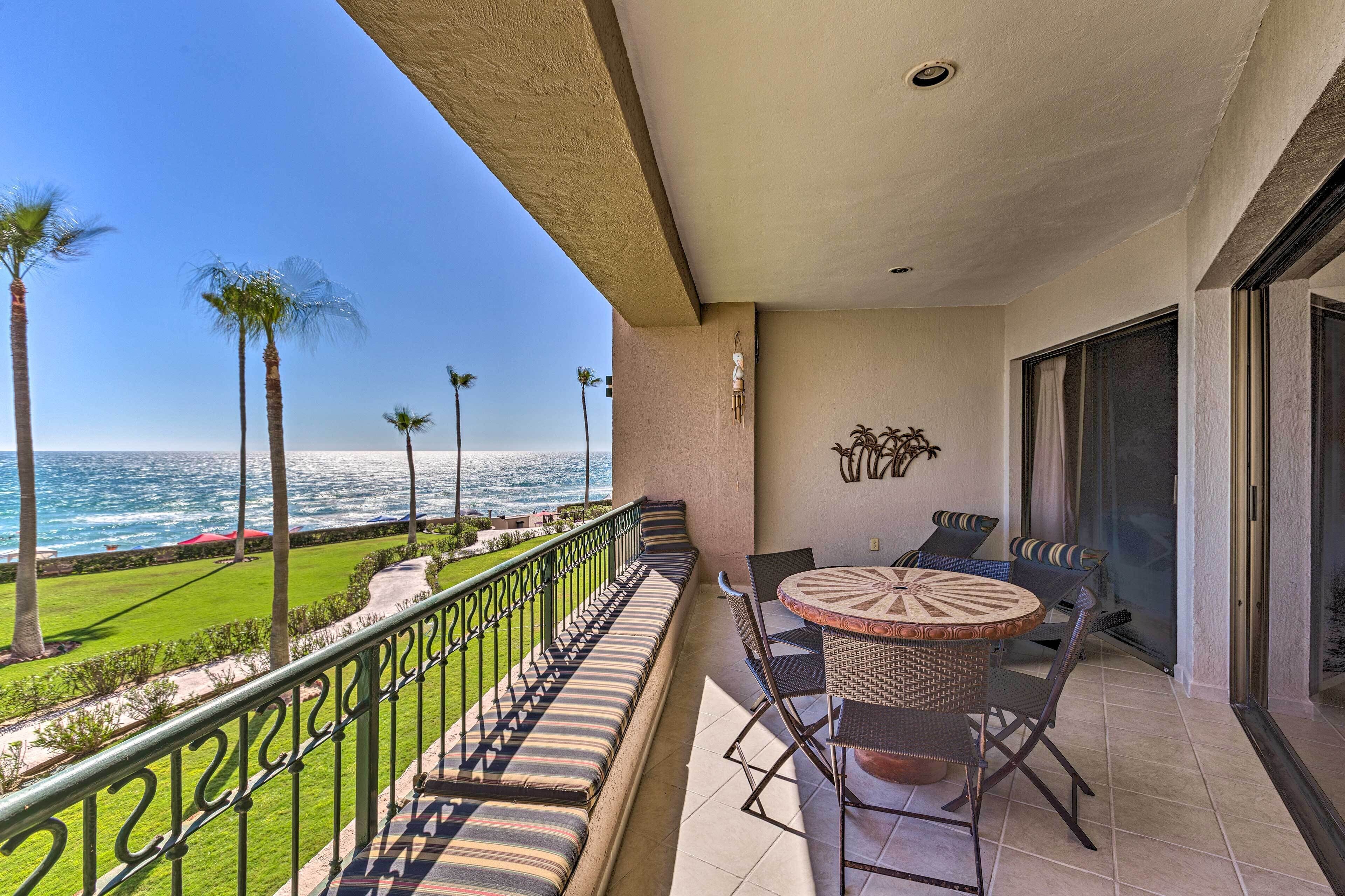 A balcony with a view of the ocean, a seating area with a table, and a railing.