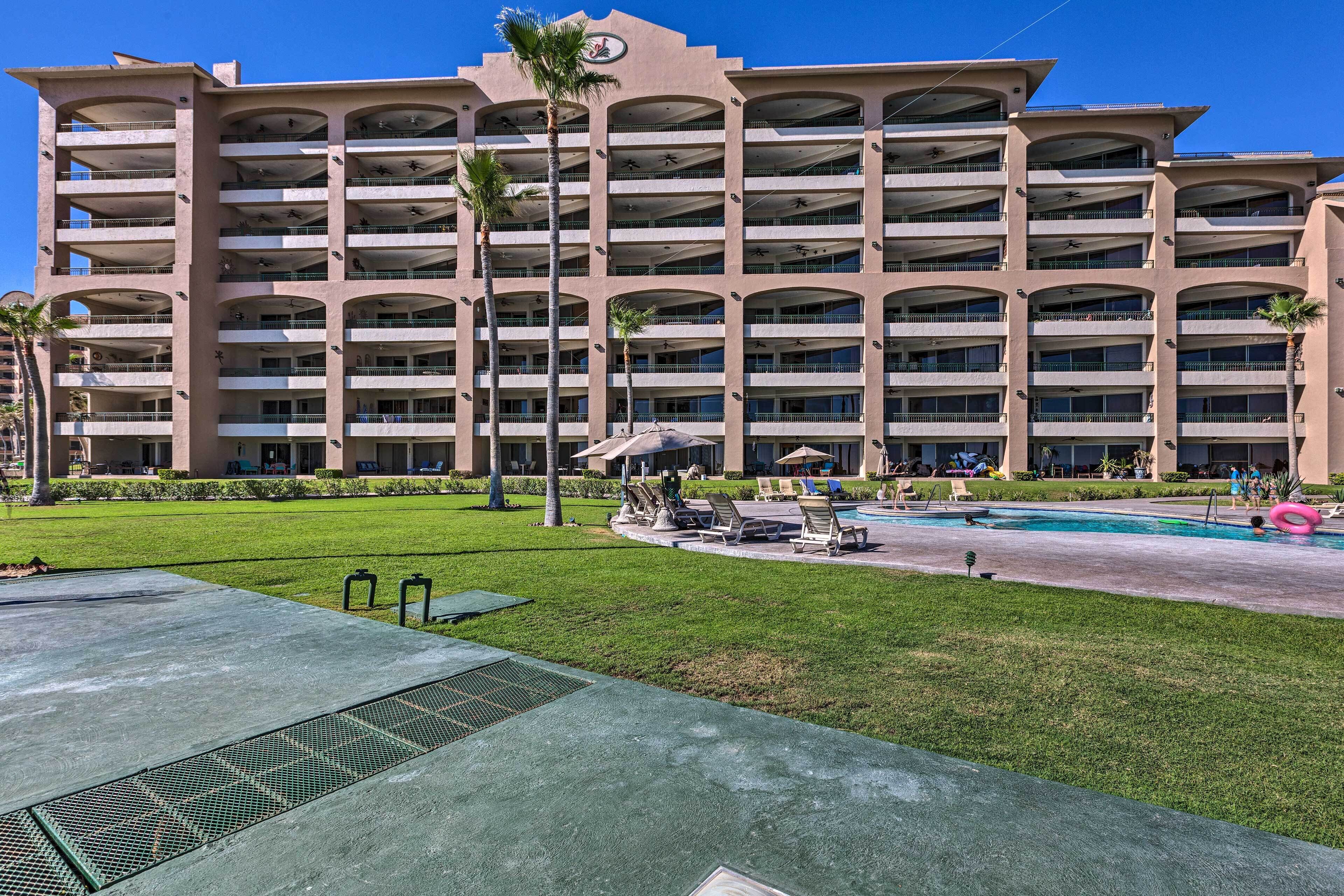 Et hotel med flere etager, et poolområde, udendørs siddepladser og palmer.