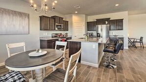 A modern kitchen with dark wooden cabinets, a central island with bar stools, a dining table with chairs, and a chandelier. - Inviting Sahuarita Home < 5 Mi to Lake Park! (Sahuarita)