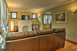 Una sala de estar con chimenea, sofá de cuero, televisor y cuadros enmarcados.