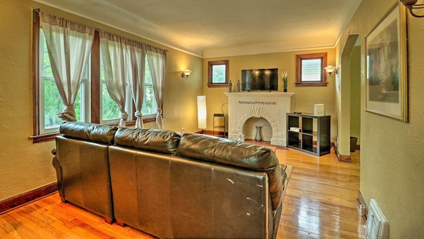 A living room with a leather sofa, a fireplace, a television, and a bookshelf. - Cozy Duplex: Half Mi to Magic Bag & Woodward Ave! (Ferndale)