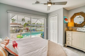 A bedroom with a large bed, a ceiling fan, a view of a swimming pool, and a white dresser with a mirror.