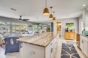 A modern kitchen with a marble countertop, white cabinets, and pendant lighting.