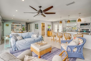 A spacious living area with a sofa, ottoman, wicker chairs, and a dining set.