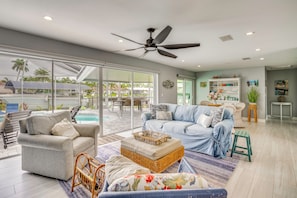 A spacious living area with a large window, a ceiling fan, and a pool view.