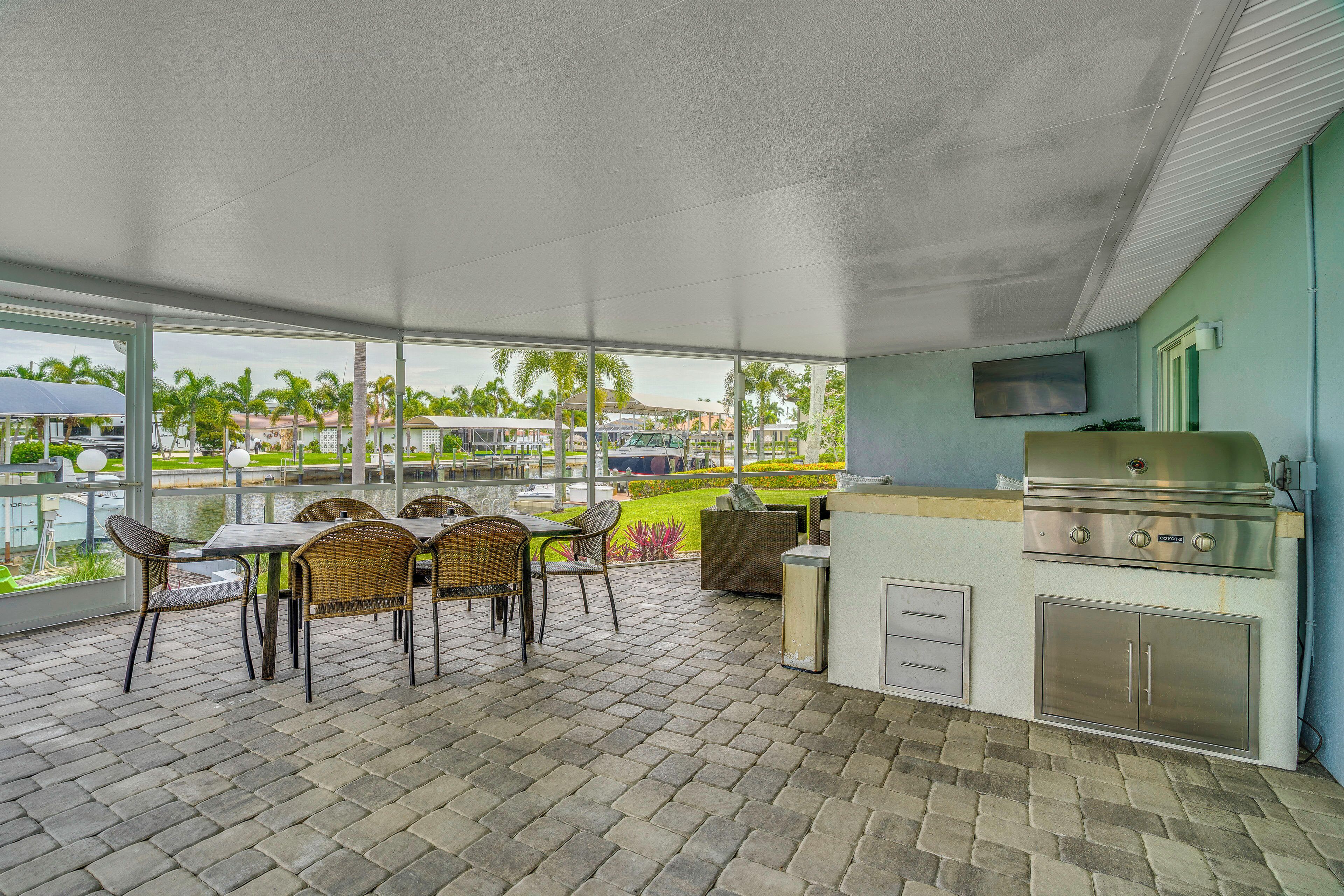 An outdoor patio with a grill, dining area, and large windows overlooking a landscaped area.