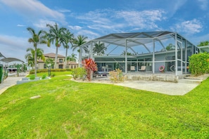 A modern glass structure with a roof, surrounded by a well-maintained lawn and palm trees.